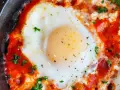 Uova al pomodoro, un piatto saporito con uovo cotto in salsa di pomodoro e formaggio, guarnito con prezzemolo fresco.