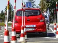 Czerwony Hyundai na placu manewrowym, z literą "L" na dachu. Instruktor pokazuje znak pokoju. Przygotowania do egzaminu na prawo jazdy b+e.