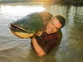 Ein Mann hält stolz einen riesigen Wels im Wasser. Ein erfolgreicher Tag beim Angeln auf Wels!
