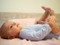 Uśmiechnięte, 5 miesięczne dziecko leży na plecach, podnosząc nóżki do góry.