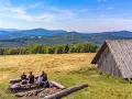 Rodzina odpoczywa na ławce przy ognisku na hali jaworowej, podziwiając górski krajobraz.