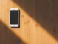 Biały smartfon leży na drewnianym blacie. Słońce rzuca cień. Jak namierzyć telefon, gdy zaginie?