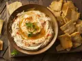 Houmous crémeux, garni de paprika et de persil, servi avec des chips pita croustillantes. Une recette houmous facile pour un apéritif gourmand.