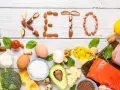 Słowa "KETO" ułożone z orzechów i nasion. Wokół składniki diety keto: ryba, mięso, jajka, awokado, olej, ser, warzywa.