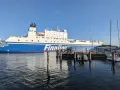 Duży prom Finnlines "Finntrader Malmö" cumuje w porcie, gotowy do rejsu. W tle widać żaglówki. Prom do Finlandii czeka na pasażerów.