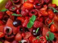 Macedonia di frutta fresca e colorata: fragole, ciliegie, lamponi e anguria, guarnita con foglie di menta.