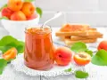 Tarro de mermelada de albaricoque casera, con tostadas y albaricoques frescos alrededor.