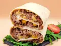 Pyszna tortilla z mięsem mielonym, kukurydzą i serem, przekrojona na pół, z rukolą i pomidorkiem.