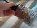 Mano aplica pintura con un pincel seco sobre listones de madera.