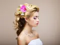 Elegancka, naturalna fryzura na wesele z lokami i kwiatami. Delikatne fale i ozdoby podkreślają urodę panny młodej.