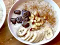 Un tazón de avena cremosa, perfecto para aprender como hacer porridge. Decorado con rodajas de plátano, trocitos de manzana, canela y un toque de chocolate derretido.