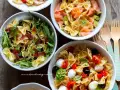 Tre ciotole di pasta fredda saporita: una con salmone e avocado, una con rucola e prosciutto, e una con pomodorini, mozzarelline e olive.