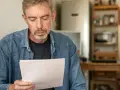 Ein Mann mit grau meliertem Haar und Bart blickt nachdenklich auf ein Dokument. Er sucht verzweifelt nach seinem Scheidungsurteil, das er verloren hat.