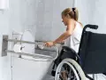 Młoda kobieta w wózku inwalidzkim korzysta z uchwytów przy toalecie. Czy można odliczyć remont łazienki od podatku?