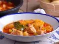 Bol de patatas con bonito en salsa roja, decorado con hojas de laurel.