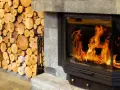 Leña apilada junto a una moderna insert chimenea con llamas danzantes.