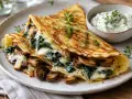 Herzhafte Pfannkuchen gefüllt mit Spinat und Pilzen, überbacken mit Käse, serviert mit Kräuterquark.