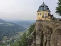 Żółty pałac na skale, część twierdzy Königstein, góruje nad doliną rzeki i lasami.