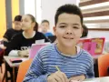 Uśmiechnięty chłopiec w swetrze, piszący w klasie. To ważny etap rozwoju 6 latka, nauka i nowe doświadczenia.