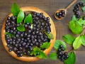 Frische Aroniabeeren in einer Holzschale und auf einem Löffel, bereit zum Verarbeiten.