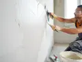Un ouvrier applique un enduit sur un mur humide avec une truelle et une taloche. Le travail progresse, laissant une surface lisse.