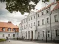 Elegancki pałac Zwartowo z białymi zdobieniami i łukowym wejściem. Na pierwszym planie para spaceruje po brukowanym dziedzińcu.