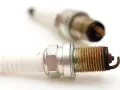 Two used spark plugs for cars, showing wear and tear on their metal tips.