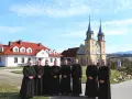 Grupa księży w czarnych szatach przed żółtym kościołem. Czy to miejsce, gdzie zbierany jest podatek na kościół?