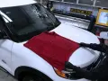 Person in gloves carefully places a plush red towel on a white car hood, demonstrating the best way to wash a car without scratching.