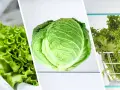 Trzy rodzaje zielonych warzyw: sałata masłowa w folii, główka kapusty i sałata lodowa w koszyku.
