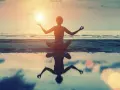 Frau in Lotusposition am Strand bei Sonnenuntergang. Ihre Meditation stärkt das Selbstbewusstsein.