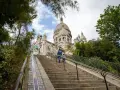 Dwie osoby wspinają się po schodach na wzgórze Montmartre, w tle Bazylika Sacré-Cœur.