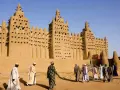 La grande mosquée de Djenné, chef-d'œuvre d'architecture en terre, se dresse sous un ciel bleu. Des hommes en tenues traditionnelles s'approchent, ajoutant vie à ce site historique.