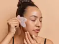 Frau mit geschlossenen Augen nutzt ein Gua Sha Stein zur Gesichtsmassage. Ob morgens oder abends, die Anwendung belebt die Haut.