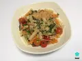 Pasta tricolor con tomates cherry, albahaca y queso rallado en un plato blanco.