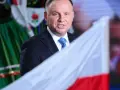 Prezydent Andrzej Duda w garniturze i krawacie, na tle polskiej flagi i tradycyjnego stroju. Ile trwa ułaskawienie prezydenta?