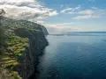 Widok na klifowe wybrzeże z domkami na zboczu i farmą rybną na oceanie. Zastanawiasz się, ile leci się na Maderę?