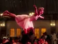 Ikoniczna scena z filmu tanecznego: mężczyzna unosi kobietę w różowej sukience w powietrze.