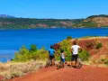 Famille à vélo profitant d'une randonnée au lac du Salagou, avec ses eaux bleues et ses collines rouges.
