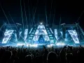 Eine riesige Menge jubelt bei einem EDM-Konzert. Die Bühne ist mit geometrischen Mustern und blauen Lichtern beleuchtet, was die Bedeutung von EDM-Musik für die Fans unterstreicht.