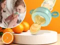 Mama karmi dziecko smoczkiem do owoców, który wygląda jak mały dzbanuszek z pomarańczowym płynem. Obok pomarańcze.