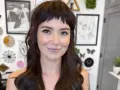 Uśmiechnięta kobieta z ciemnymi włosami i grzywką baby bangs.