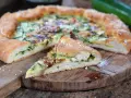 Leckeres Zucchini Pizza Rezept auf einem Holzbrett, mit einem Stück abgetrennt.