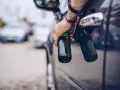 Mann hält zwei Bierflaschen aus dem Autofenster. Er versucht, den Alkohol abzubauen, indem er sie wegwirft.