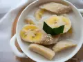 Kawałki banana w mleku kokosowym, ozdobione liściem pandanu i sezamem. Pyszny tajski deser.