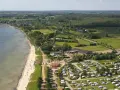 Luftaufnahme eines Campingplatzes in Schleswig-Holstein mit Wohnmobilen und Zelten, direkt am sandigen Strand und dem Meer gelegen.