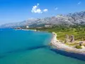 Piękne wybrzeże z górami w tle, idealne na camping Paklenica. Woda kusi turkusowym kolorem, a na plaży widać ruiny starej twierdzy.