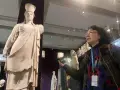 A woman with a museum pass for Turkey gestures towards a marble statue of a woman in a museum.
