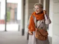 Elegancka kobieta w płaszczu w drobną kratę i pomarańczowym szalu. Czy krata pogrubia? Ten styl pokazuje, że niekoniecznie!