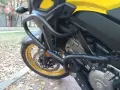 Żółty motocykl z czarnymi gmolami chroniącymi silnik i osłony. Złota obręcz koła i tarcza hamulcowa.